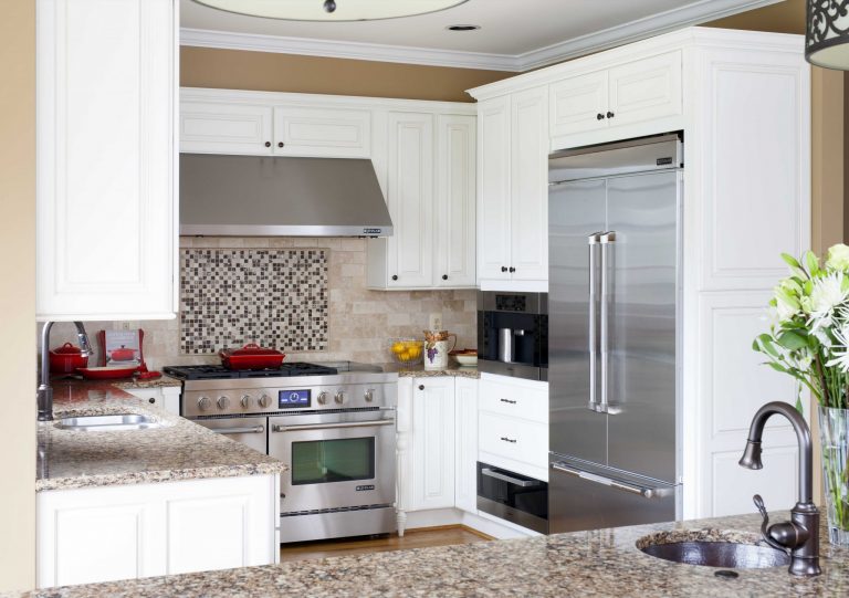 renovated traditional style kitchen white cabinetry mosaic tile detail in backsplash stainless steel appliances and range hood crown molding recessed lighting