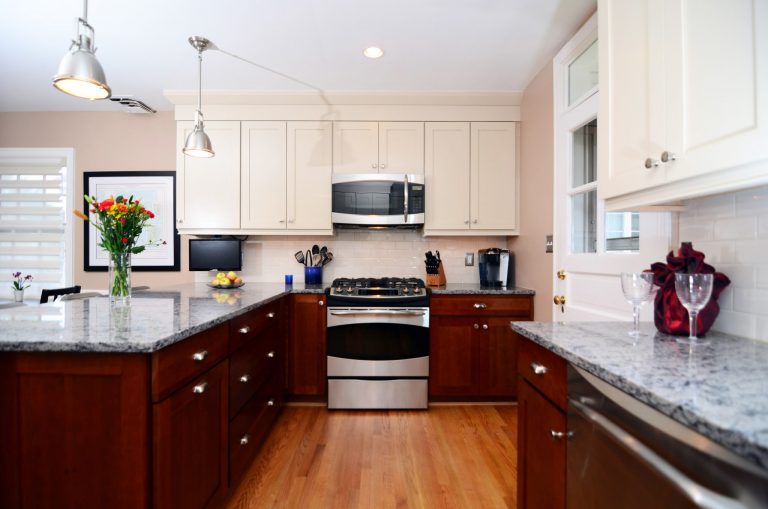 traditional style kitchen with wood floors dark lower cabinets white upper cabinets peninsula and stainless steel appliances recessed and pendant lighting