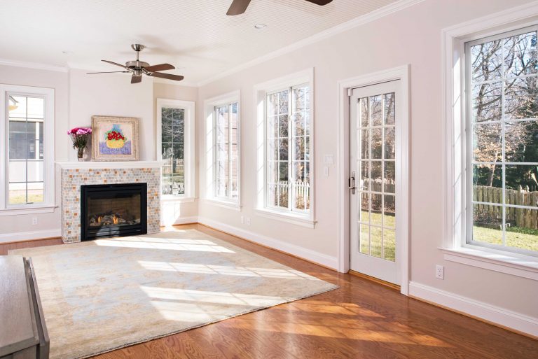 updated living room in traditional maryland home glass door large windows ceiling fan wood floors fireplace crown molding bright peachy color palette