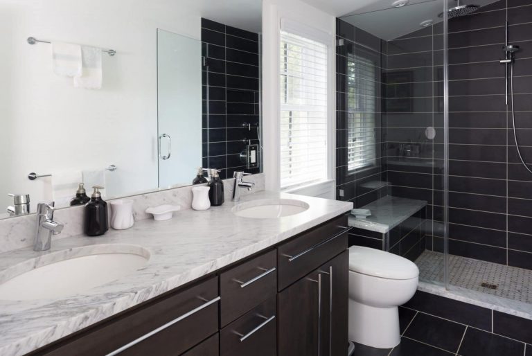 vanity with double sinks separate shower stall with glass door and built in bench black tile