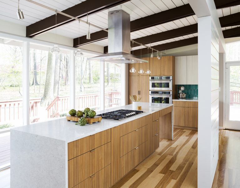 modern kitchen natural wood cabinetry and floors waterfall edge countertops teal tile backsplash beam ceiling