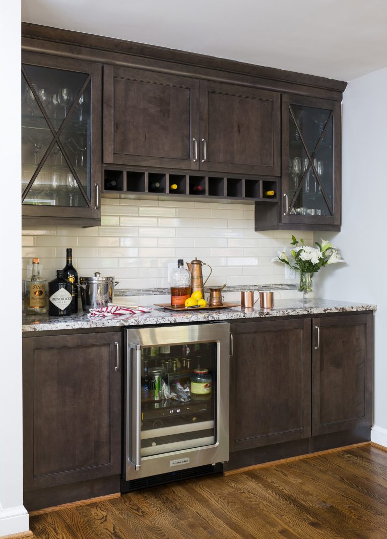 bar area dark wood cabinetry glass door upper cabinets beverage refrigerator subway tile backsplash