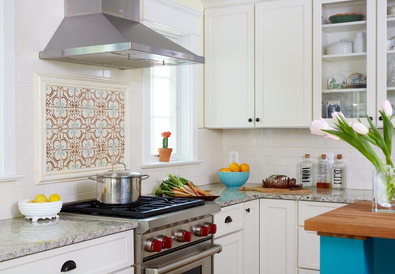 kitchen with white outer cabinetry and teal island cabinetry teal and orange mosaic tile backsplash behind stainless steel gas range