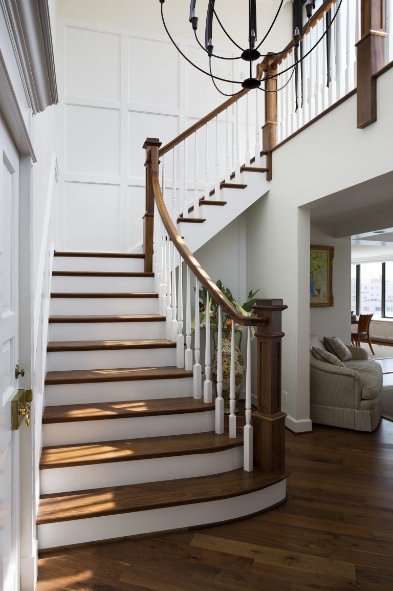 staircase with wooden banister white paneled walls and eclectic chandelier