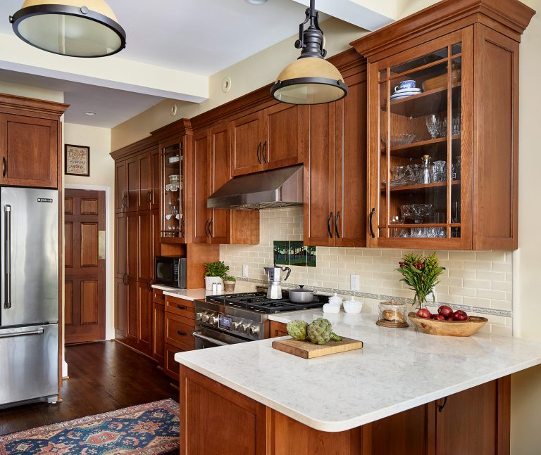 case design kitchen with rich dark wood finish cabinets with pull black handles, corner kitchen island with marble counter and hanging pendant light